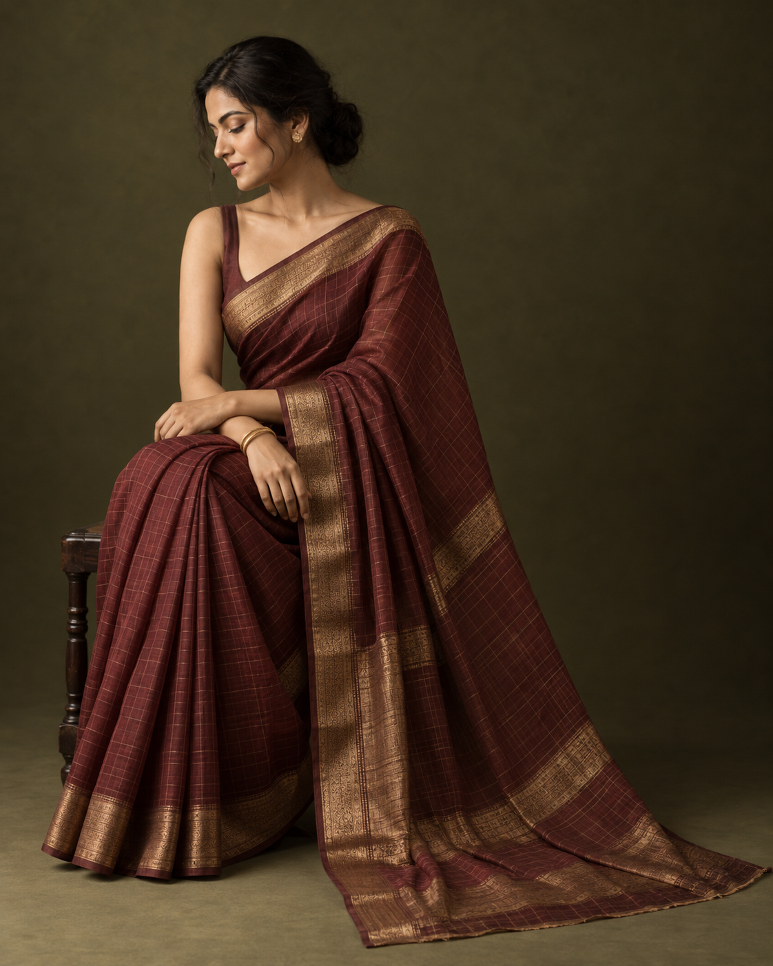 Woman seated in a maroon handloom saree with a wide gold zari border